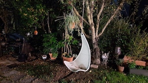 A hanging chair suspended from a tree, surrounded by potted plants and a garden setting.