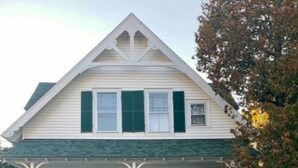 Una casa de dos pisos con un porche, contraventanas verdes y fachada blanca.