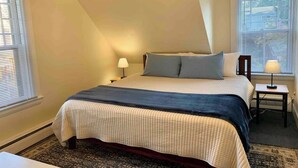 Un dormitorio con una cama, dos mesitas de noche y un ventanal con persianas.