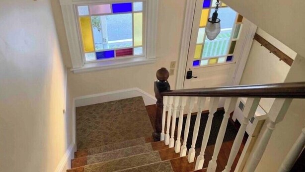 Una escalera con balaustres blancos y barandilla de madera que conduce a una habitación con un ventanal de vidrios multicolores.