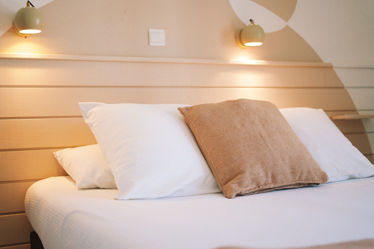 A neatly made bed with white and brown pillows, two wall-mounted lamps, and a headboard with horizontal lines.