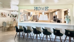 Een receptiebalie met een 'WELCOME'-bord, een bar met krukken, een eetgedeelte met stoelen en een keuken op de achtergrond.