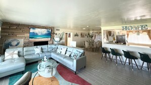 Een moderne woonkamer met een hoekbank, een glazen salontafel en een eethoek met een bar.