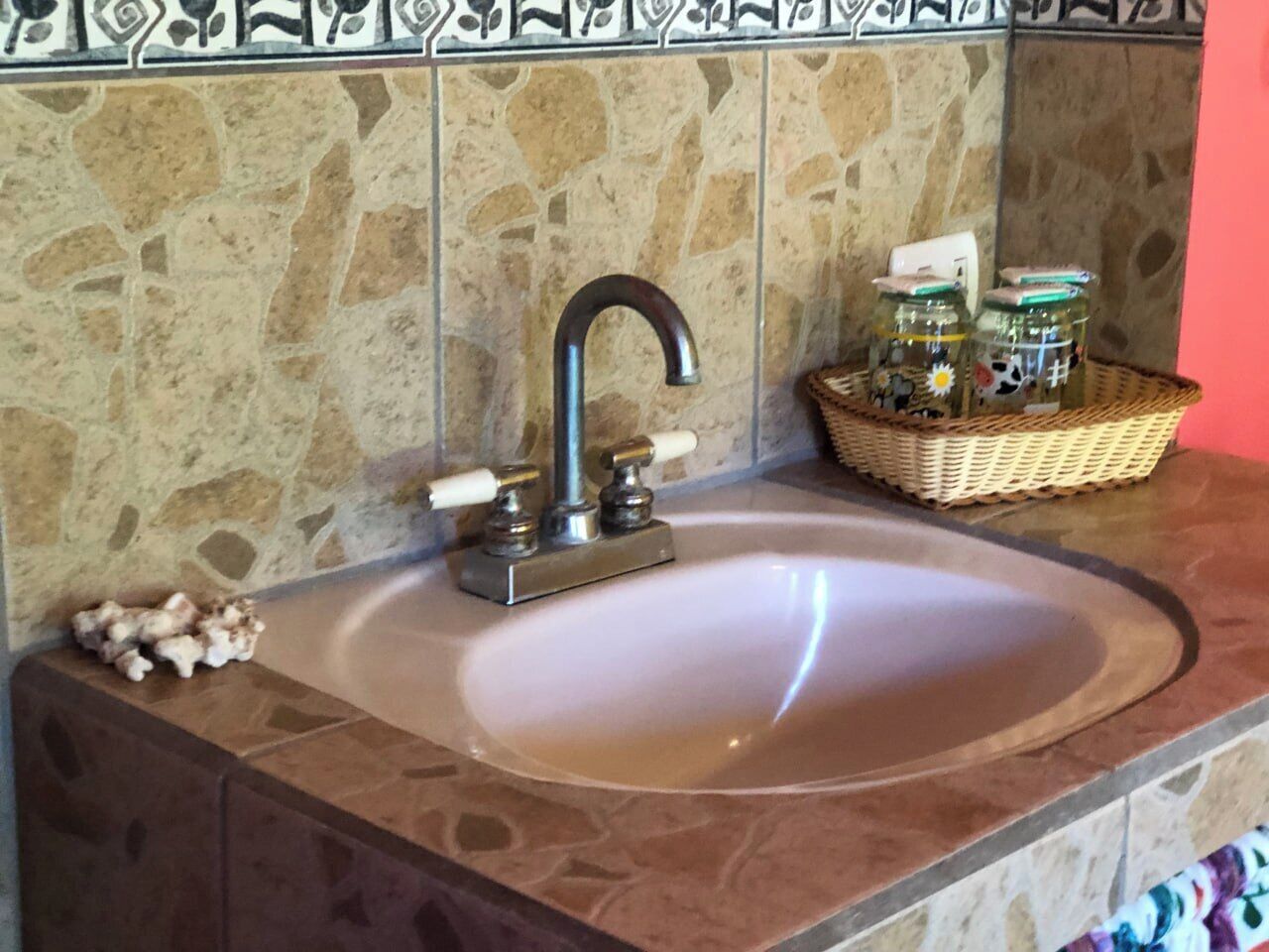 A bathroom sink with a modern faucet, a stone tile backsplash, and a wicker basket with jars on the countertop.