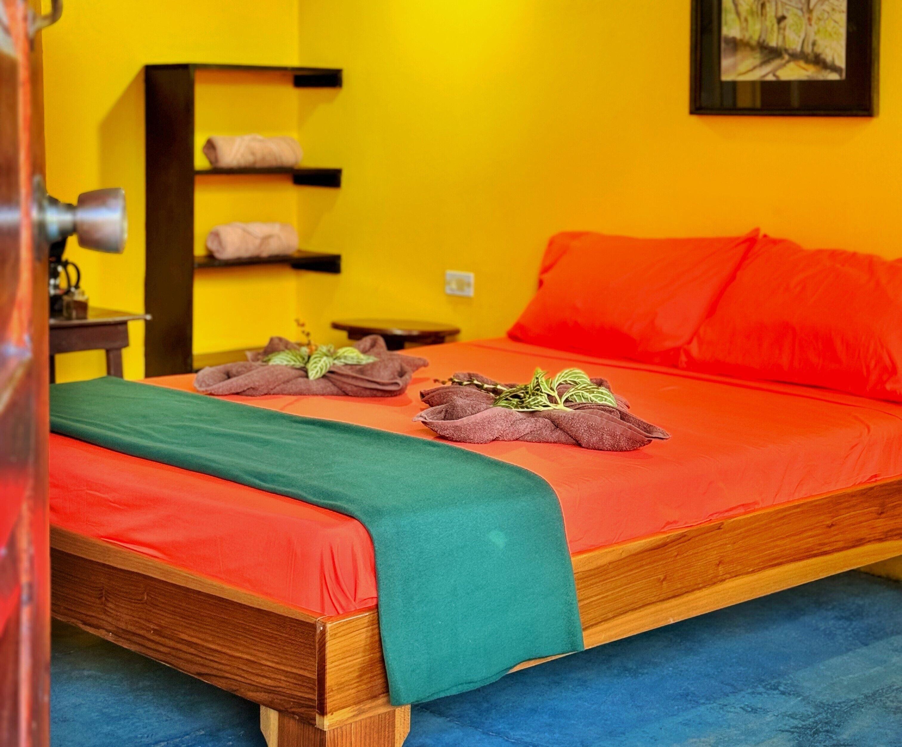 A bed with a green and red bedspread, two towels with herbs, a wooden headboard, and a yellow wall.