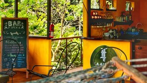 Zona de bar con menú en pizarra, mesas al aire libre y vistas a árboles.