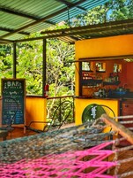 Uma área de bar com cardápio em lousa, mesas ao ar livre e vista para as árvores.