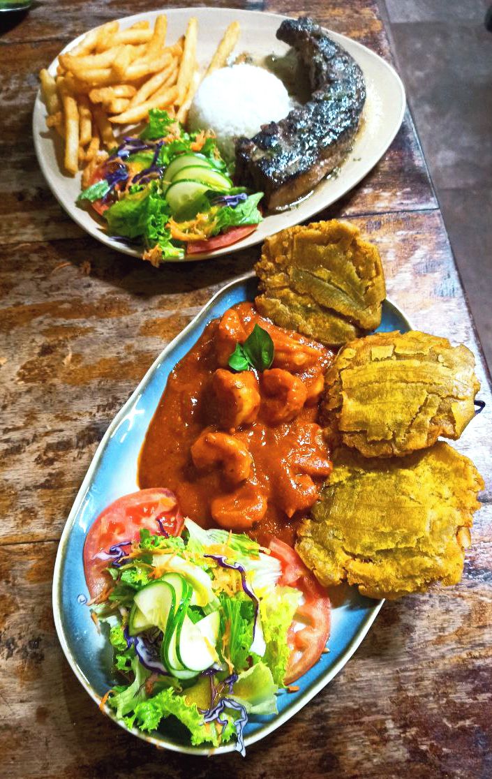 A plate with a variety of food including fries, a fish, a salad, and a side of plantains.