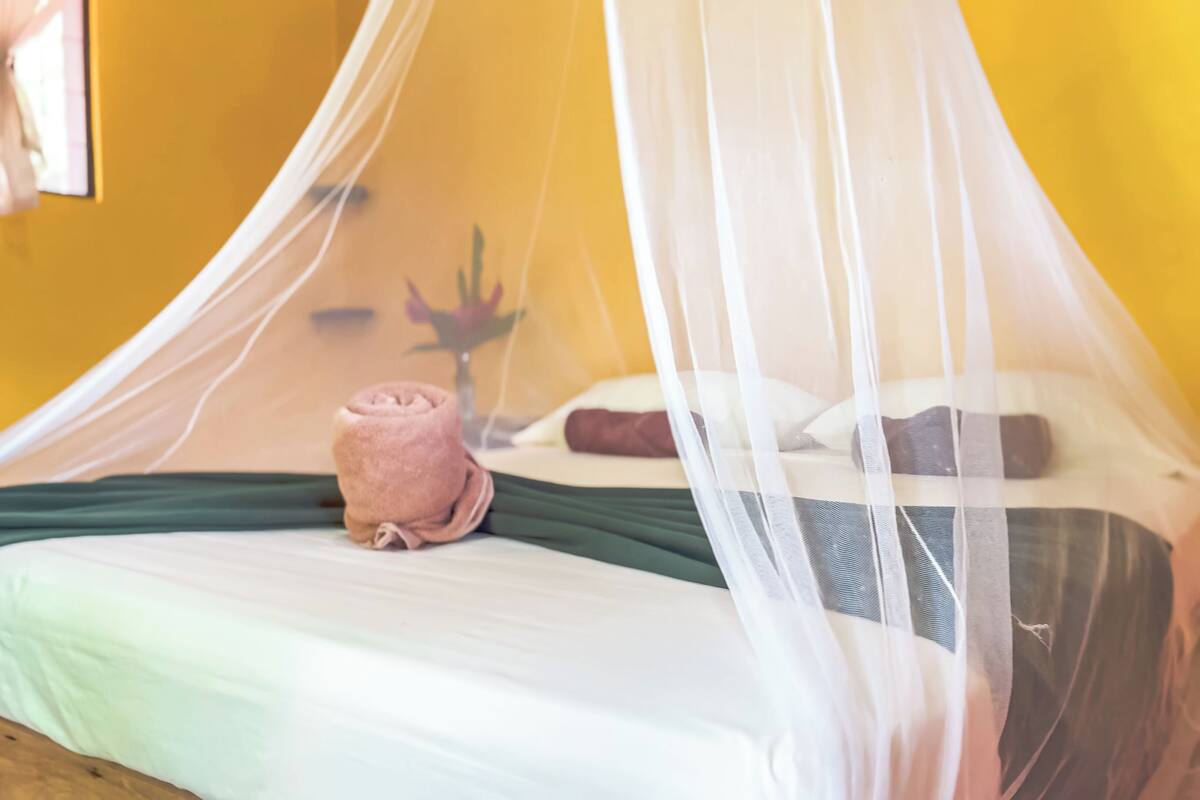 A bed with a white canopy, a green bedspread, and a pink towel.