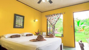 Habitación de hotel con cama, un cuadro enmarcado, una ventana con cortina y vista a un jardín.