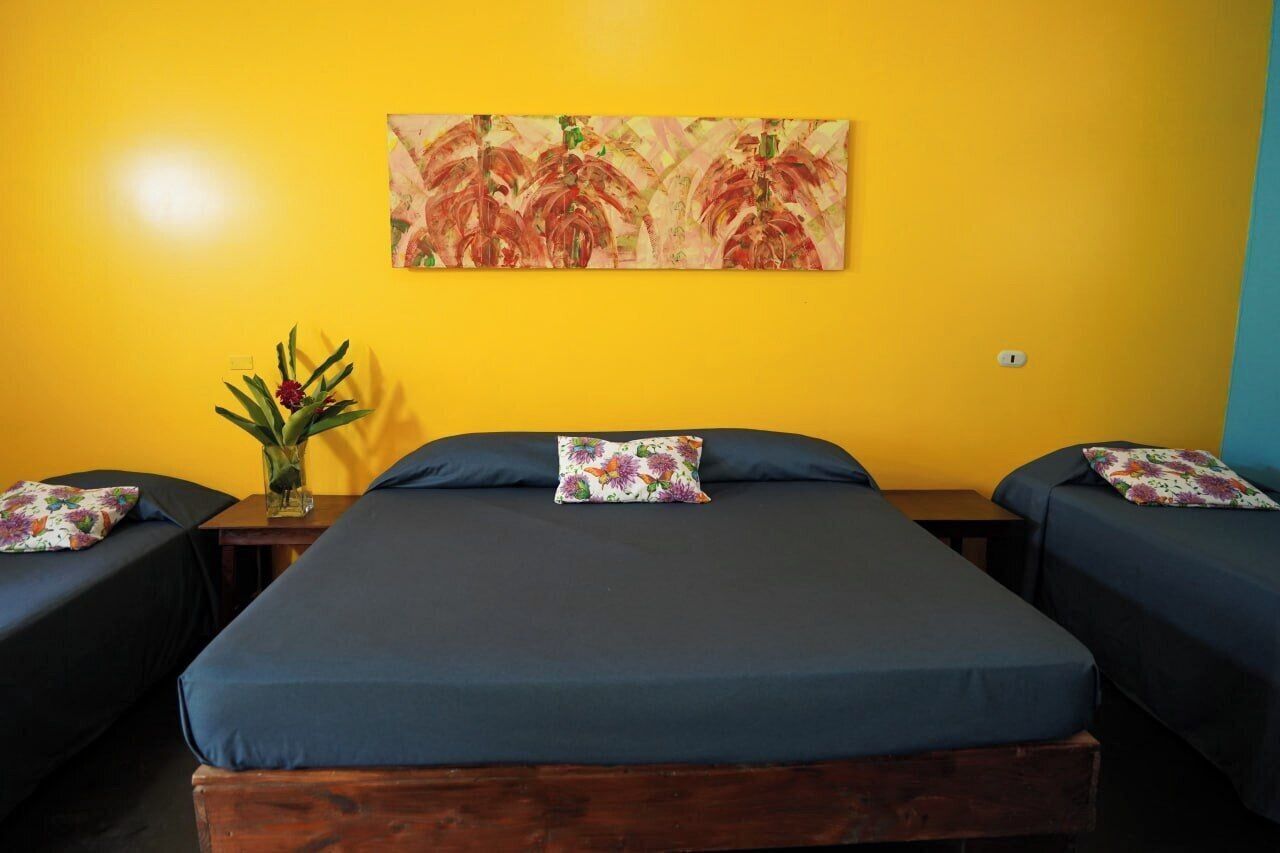 Ein Zimmer mit drei Betten, einem großen Gemälde an der Wand und einem kleinen Tisch mit Blumen.