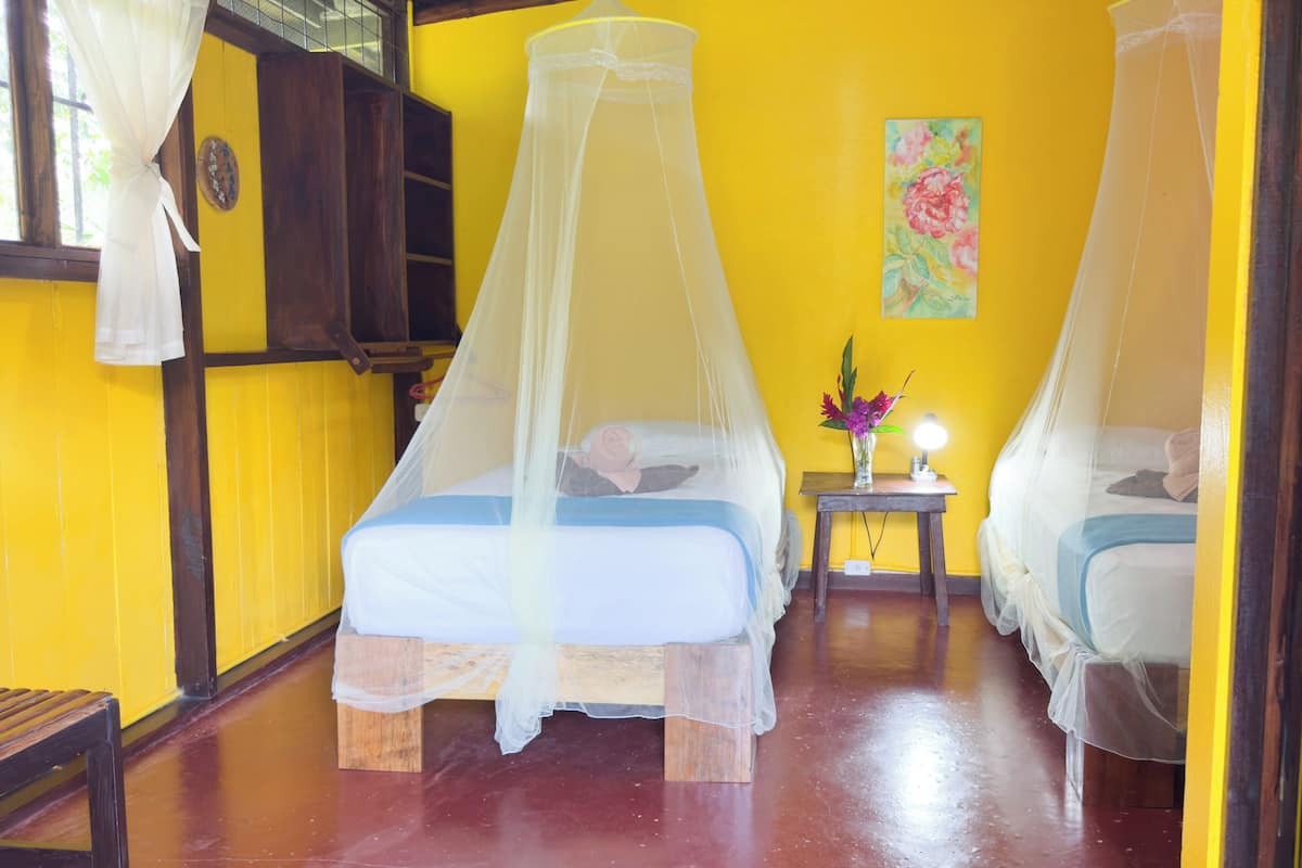 A room with two beds, each with a canopy, a small table with a lamp, and a painting on the wall.