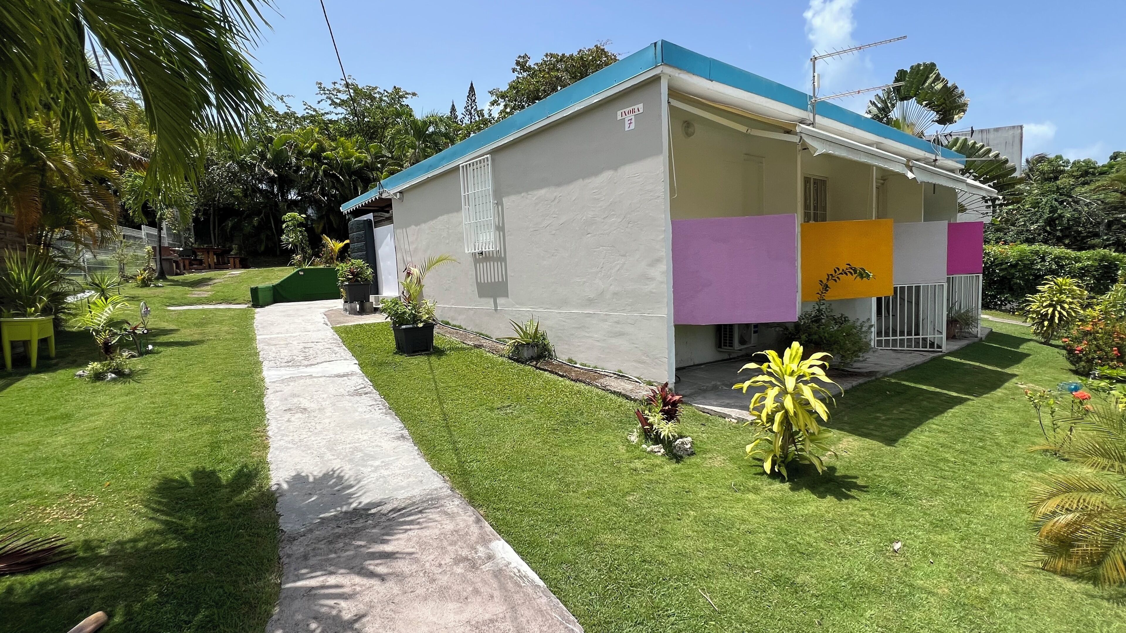 A single-story building with a flat roof, a concrete pathway leading to the entrance, and a well-maintained lawn with various plants.