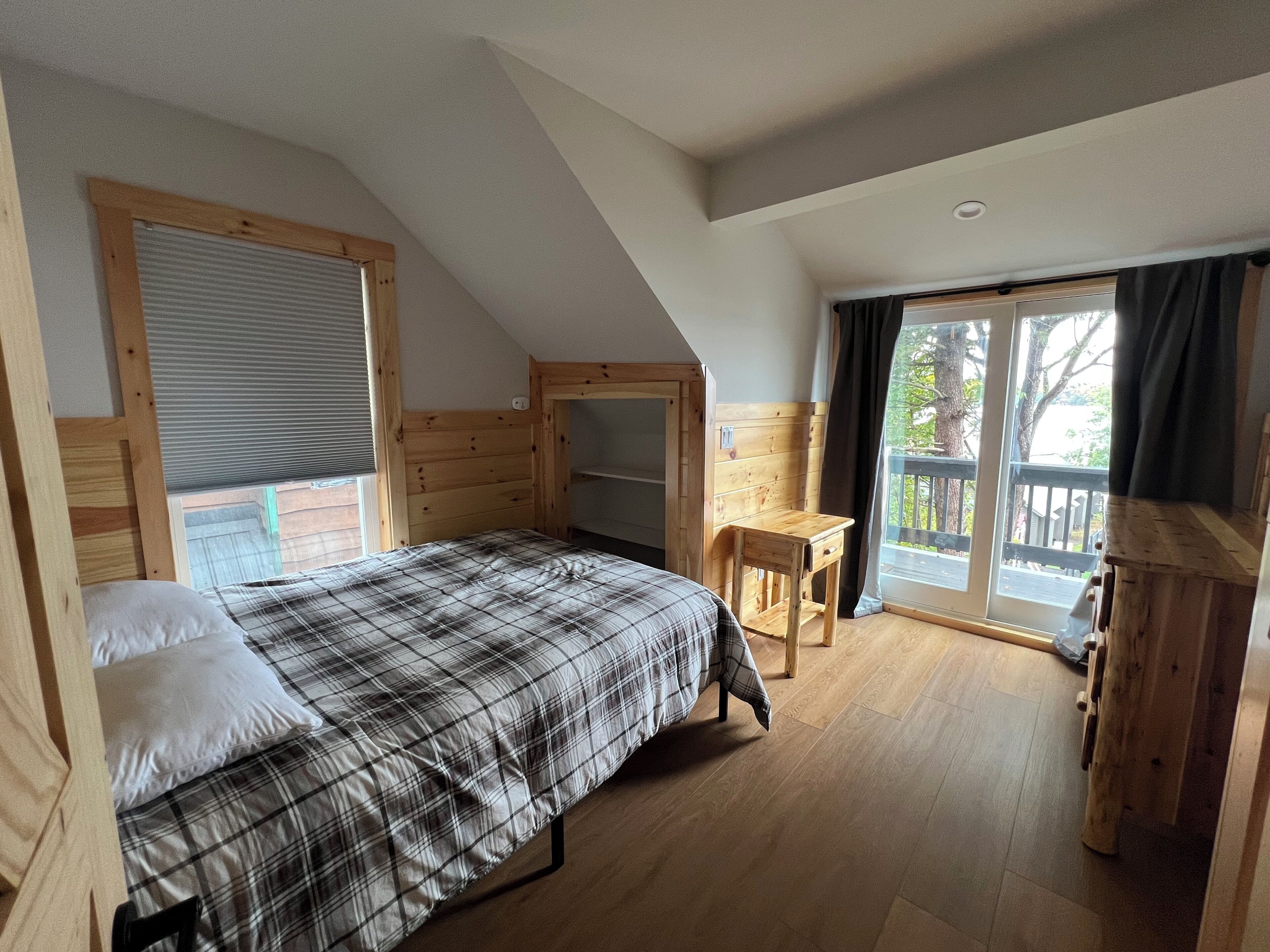 A cozy bedroom with a bed, a wooden desk, and a large window.