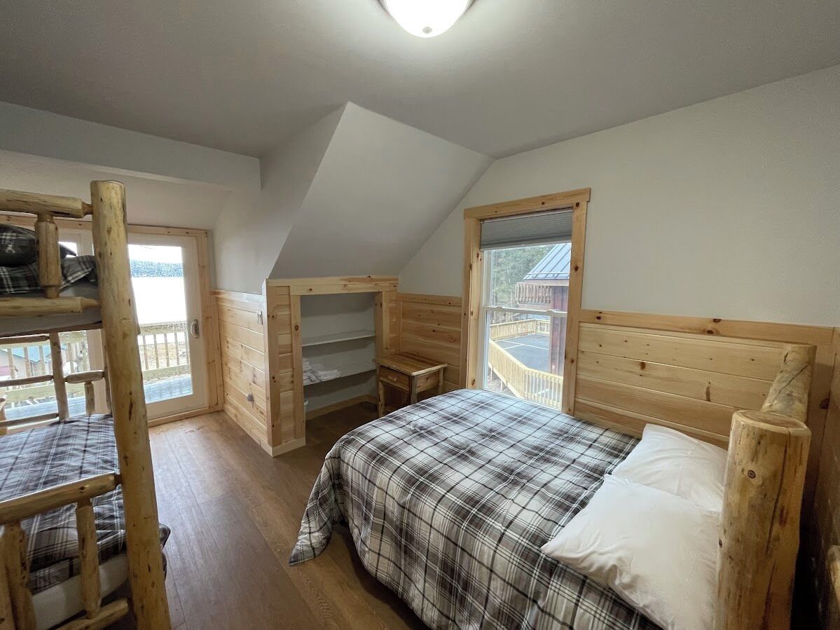 Une chambre de type dortoir, avec des lits superposés, un bureau en bois et une fenêtre donnant sur un balcon.