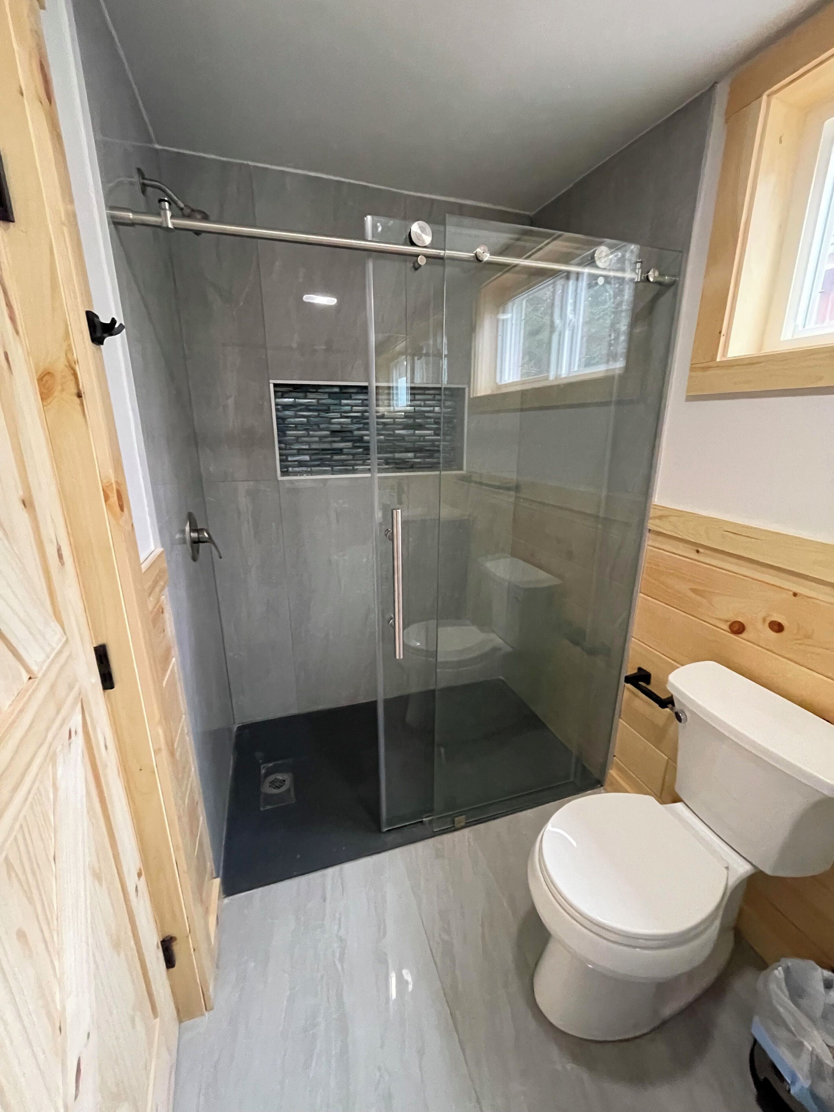 A modern bathroom with a glass-enclosed shower, a toilet, and a built-in sink.