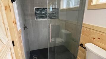 A modern bathroom with a glass-enclosed shower, a toilet, and a built-in sink.
