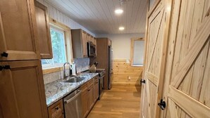 Una cocina estrecha con armarios de madera, un lavamanos de acero inoxidable y una ventana.