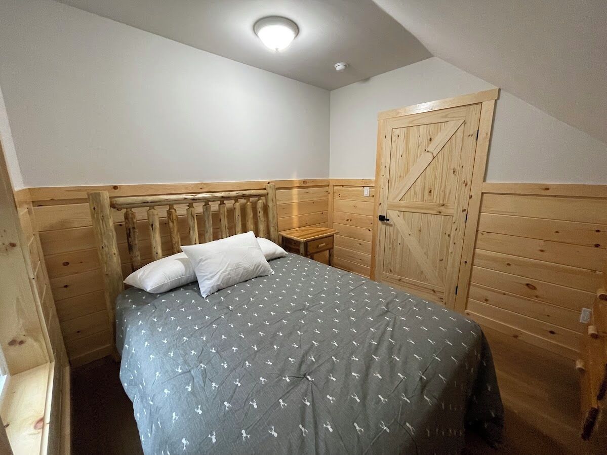 Een slaapkamer met een bed, een houten hoofdbord, een klein nachtkastje en een houten garderobe.