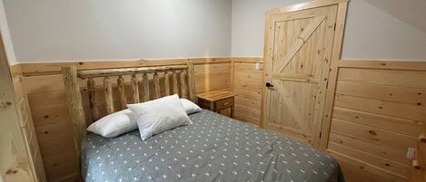Een slaapkamer met een bed, een houten hoofdbord, een klein nachtkastje en een houten garderobe.
