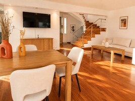 Una sala moderna con una mesa de comedor de madera, sillas blancas, un sofá y una escalera.