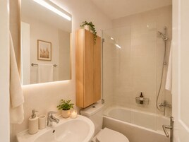 Un baño moderno con un espejo grande, un mueble de madera, un lavamanos con grifo, inodoro y zona de ducha con mampara de vidrio.