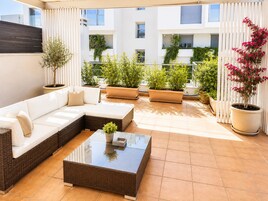 Un espacio al aire libre con luz solar, con un sofá, una mesa de centro y plantas en macetas.