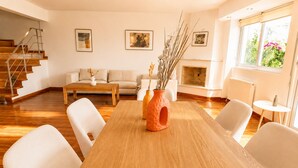 Un salon moderne avec une table à manger en bois, des chaises blanches, un canapé et une cheminée.