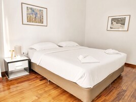 Una habitación de hotel con una cama, una mesita de noche, una lámpara y dos cuadros en las paredes.