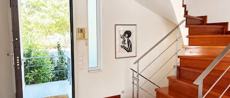 A modern interior with a wooden staircase, a door leading to a balcony, and a framed artwork on the wall.