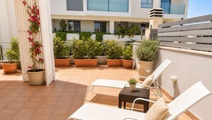 Une terrasse sur le toit, avec deux chaises longues blanches, une petite table et plusieurs plantes en pot.