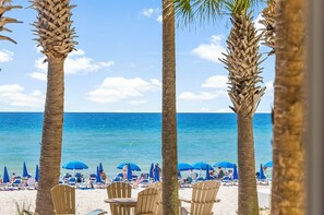 A beach with palm trees, blue umbrellas, and lounge chairs.