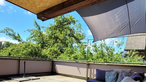 A covered outdoor seating area with a wooden deck, a cushioned sofa, and a small table. - Apartment Schöne Schwarzwald Auszeit in the hiking paradise with its own terrace (Friedenweiler)