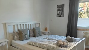 A neatly made bed with a patterned blanket and pillows, a bedside table with a lamp, and a window with curtains. - Apartment Schöne Schwarzwald Auszeit in the hiking paradise with its own terrace (Friedenweiler)