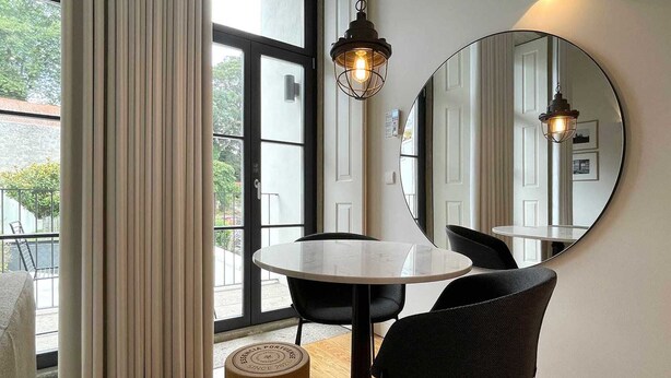 A modern dining area with a round table, two black chairs, a large mirror, and a hanging light fixture. - Studio.Ø4 Garden View (Porto)