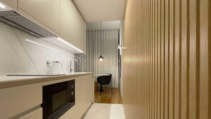 A modern kitchen with a built-in oven, a microwave, and a sink. There is a dining area with a chair and a table. - Studio.Ø4 Garden View (Porto)