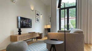 A modern living room with a sofa, a coffee table, a TV mounted on the wall, and a large window with curtains. - Studio.Ø4 Garden View (Porto)