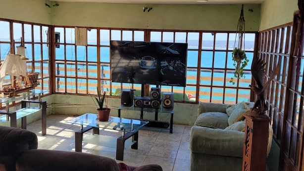 Een woonkamer met een grote televisie, een glazen salontafel en een bank. Er is uitzicht op de oceaan door grote ramen.