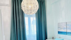 Une chambre à coucher avec un grand lit, des rideaux de couleur turquoise, un lustre et un tableau représentant un paysage marin.