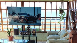 Un salon avec une grande télévision, un canapé, une table basse et une plante en pot.