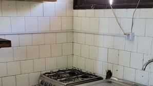 Une cuisine avec des murs recouverts de carreaux blancs, une cuisinière à gaz, un évier et des armoires en bois.