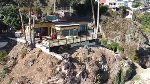 Une maison dotée d’un balcon, située sur une colline au terrain rocheux et à la végétation clairsemée.