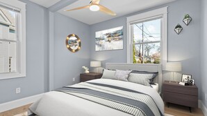 A bedroom with a bed, nightstands, a ceiling fan, a window, and wall art.