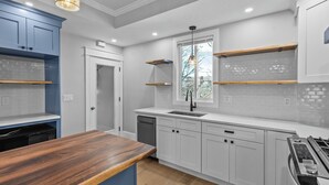 A modern kitchen with white cabinets, a wooden countertop, and a built-in dishwasher.