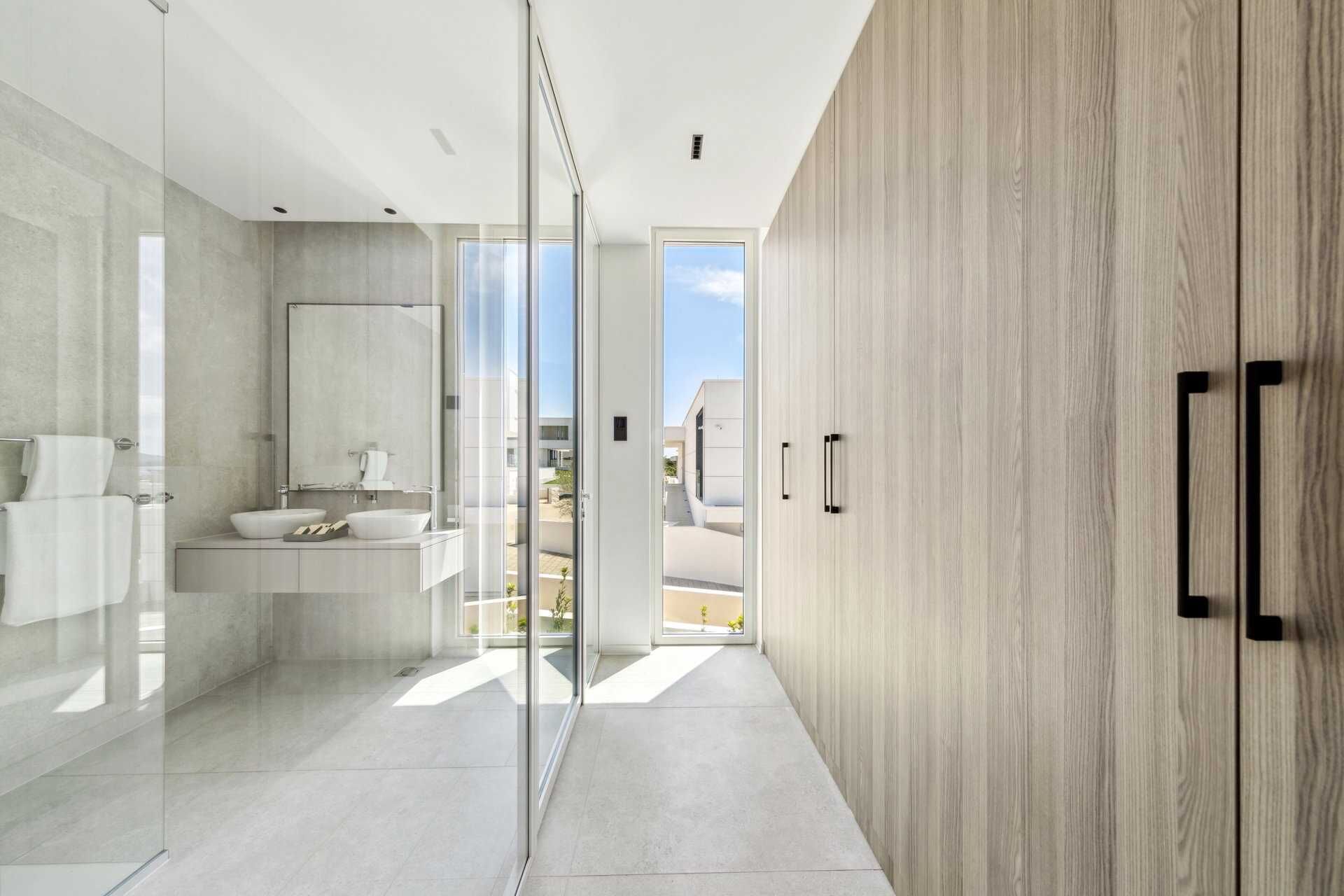 A modern bathroom with a glass shower enclosure, a large mirror, and a wooden wardrobe.