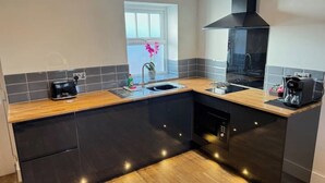 Een moderne keuken met zwarte kastjes, een houten aanrecht, een zwarte afzuigkap en een raam met uitzicht op de omgeving.
