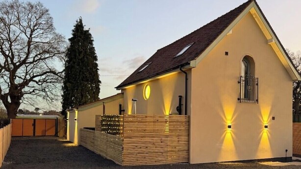 Een laag gebouw met een schuin dak, een houten hek en twee verlichte wandlampen.