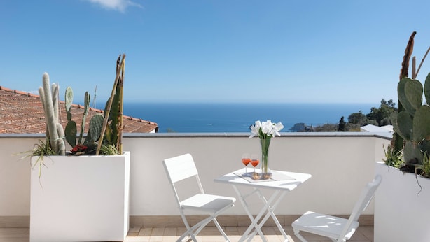 A terrace with two white chairs, a small table, and a vase of white flowers. Cacti are visible in the background.