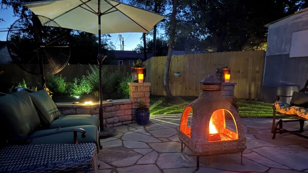 An outdoor patio with stone flooring, a stone fire pit, a wicker sofa, and an umbrella. - Midtown Cottage, unique stone patio, family-dog friendly newly remodeled. (Tulsa)