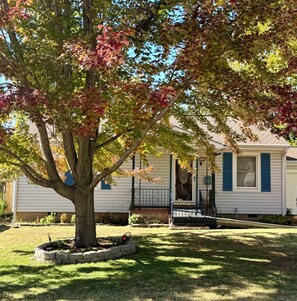 Ein Bungalow mit Veranda, ein Baum mit Herbstlaub und einem gepflegten Rasen.